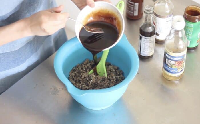 white bowl of brown sauce pouring into a blue bowl filled with ground turkey and mushrooms