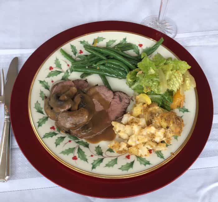 white tablecloth with christmas plate of beef and gravy, macaroni and cheese, salad, and green beans