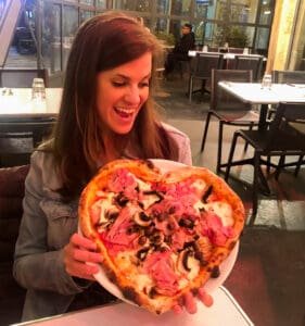 brunette female holding a heart shaped pizza in a Parisian cafe