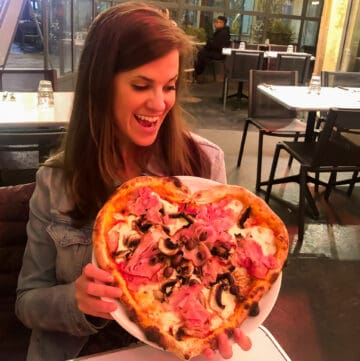 brunette female holding a heart shaped pizza in a Parisian cafe