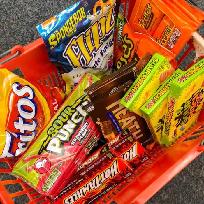red shopping basket filled with fritos, sour punch straws, hot tamales, heath bars, sour patch kids, reese's, and white chocolate covered pretzels