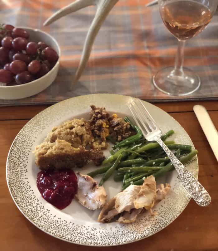 fancy china with turkey, cranberry sauce, dressing, sweet potato casserole, green beans and silver fork with rosé and grapes on table