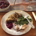 fancy china with turkey, cranberry sauce, dressing, sweet potato casserole, green beans and silver fork with rosé and grapes on table