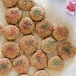 parchment paper full of baked ginger cookies with red and green sprinkles with jars of green and red sprinkles on countertop