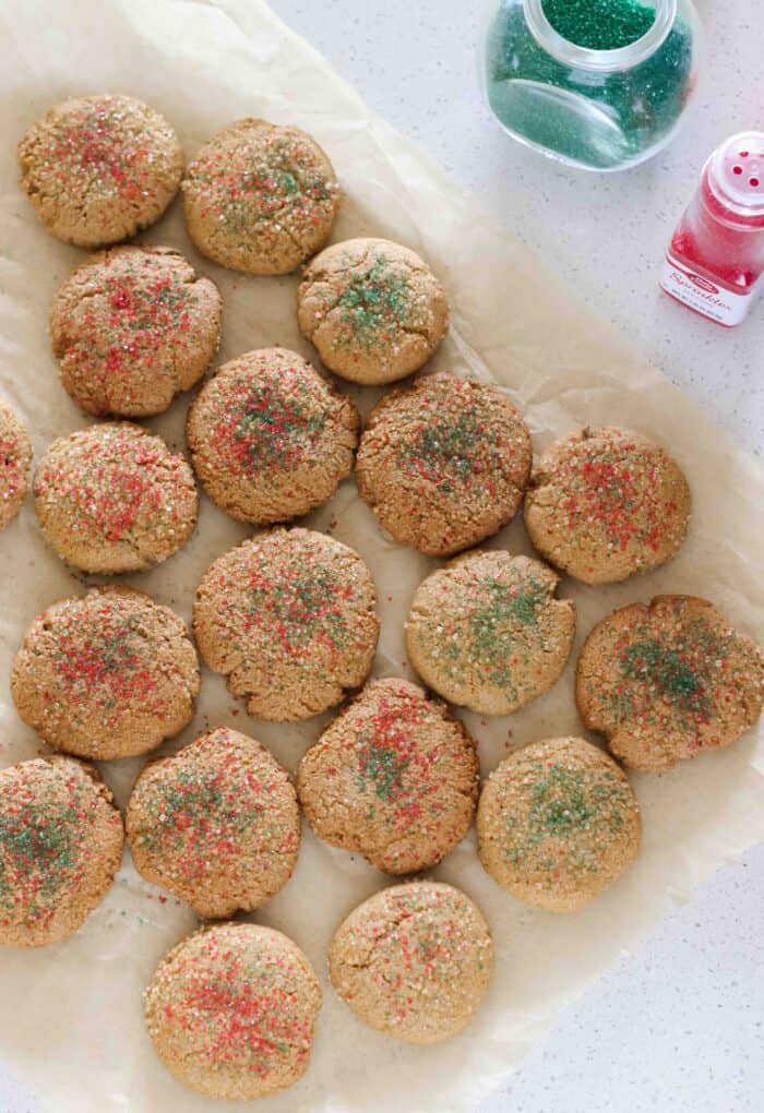 parchment paper full of baked ginger cookies with red and green sprinkles with jars of green and red sprinkles on countertop 
