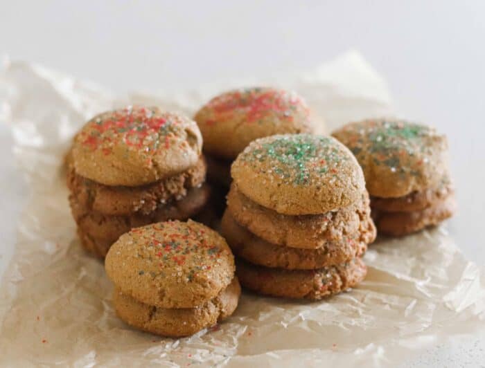 stacks of ginger cookies with green and red sprinkles on crinkled parchment paper on white countertop