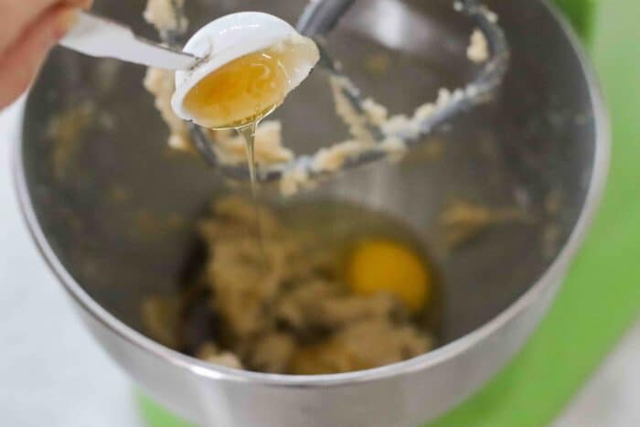 a spoon of honey drizzling into cookie dough in a green stand mixer