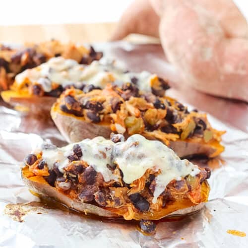 sweet potato on baking sheet with foil topped with chicken, black beans, and cheese.
