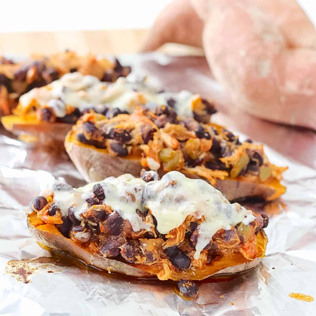 sweet potato on baking sheet with foil topped with chicken, black beans, and cheese.
