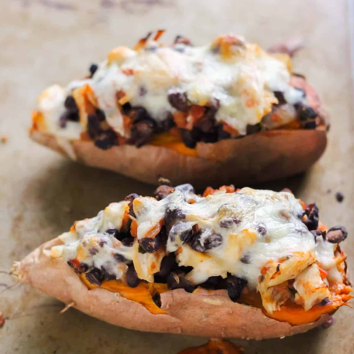 two baked sweet potatoes with beans, salsa, chicken and cheese on a baking sheet