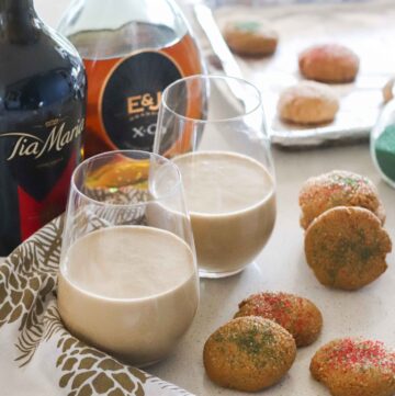 two wine glasses with coffee ice cream drinks, bottles of brandy and Tia Maria, on white and gold napkins, with Christmas cookies