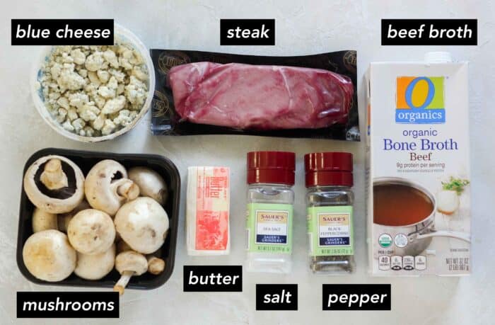 container of crumbled blue cheese, package of steak, carton of beef broth, salt, pepper, stick of butter, and container of white mushrooms with text overlay