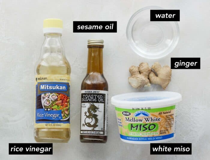 rice vinegar, sesame oil, small bowl of water, fresh ginger root, and white miso paste container on white counter