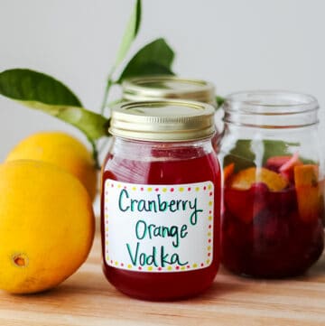 mason jars filled with cranberry infused vodka with labels on them that say "cranberry orange vodka" on a wooden cutting board with fresh oranges around the jars