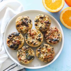 cream colored plate with veggie egg muffins on blue table with sliced oranges and a white napkin