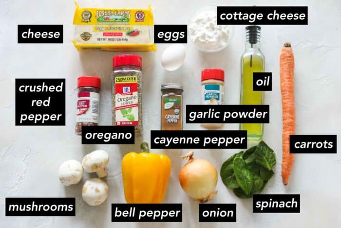 cheese, crushed red pepper, oregano, mushrooms, yellow bell pepper, onion, fresh spinach, carrot, cayenne pepper, garlic powder, eggs, oil, and a bowl of cottage cheese