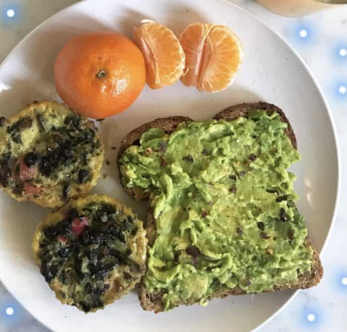 white plate with avocado toast, two spinach egg muffins, and a clementine 