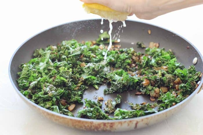 hand squeezing lemon into a skillet with wilted kale and sauteed onions