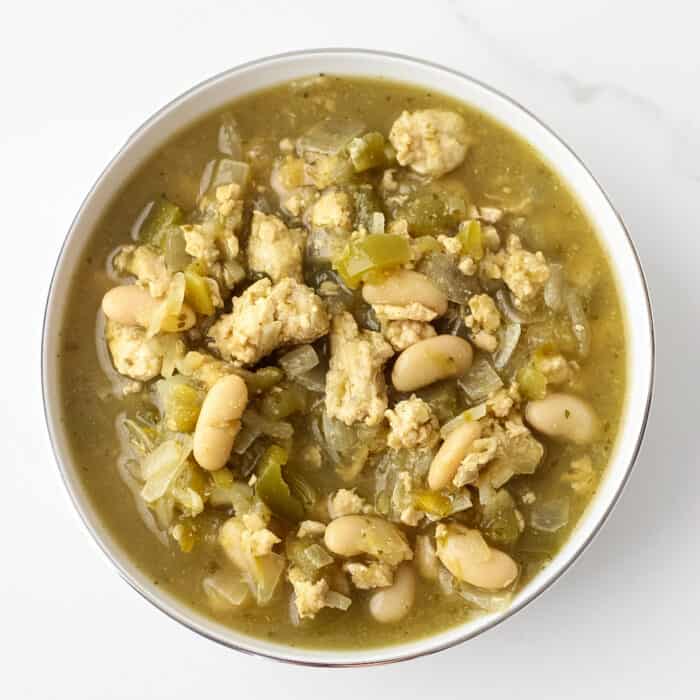 white marble counter with a white bowl of white turkey chili made with salsa verde