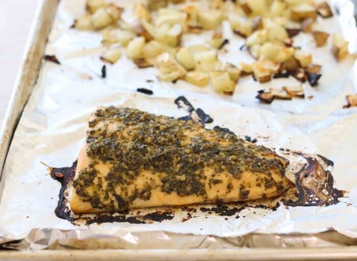 foil lined baking sheet with baked pesto salmon and roasted potatoes and onions