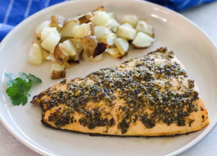 pesto salmon on a white plate with roasted potatoes and onions and parsley