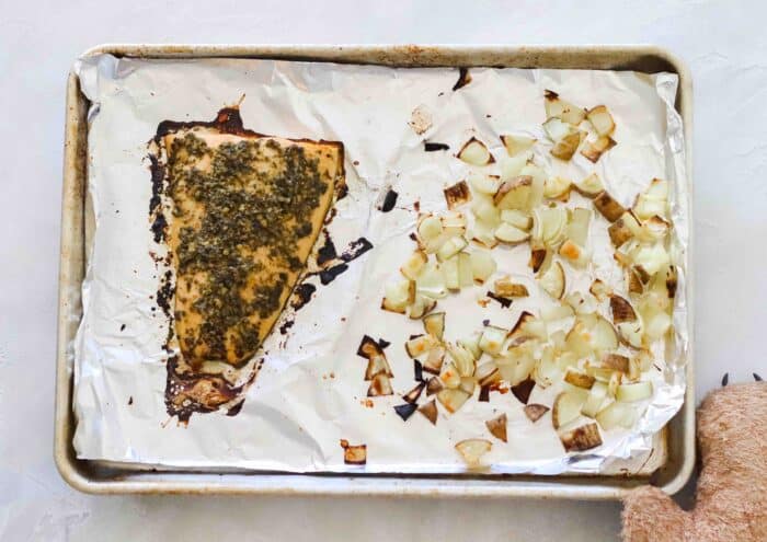 baking sheet lined with foil with baked pesto salmon, roasted potatoes and onions