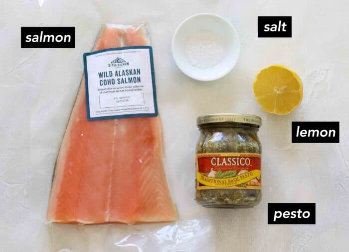 salmon fillet, small white bowl with salt, cut lemon, and a jar of pesto