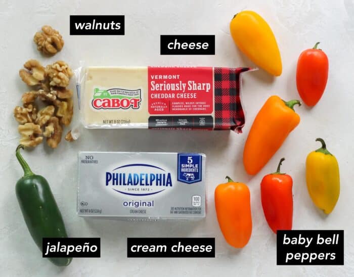 walnuts, jalapeno, block of cheddar cheese, block of cream cheese, and orange, yellow, and red baby bell peppers on white counter