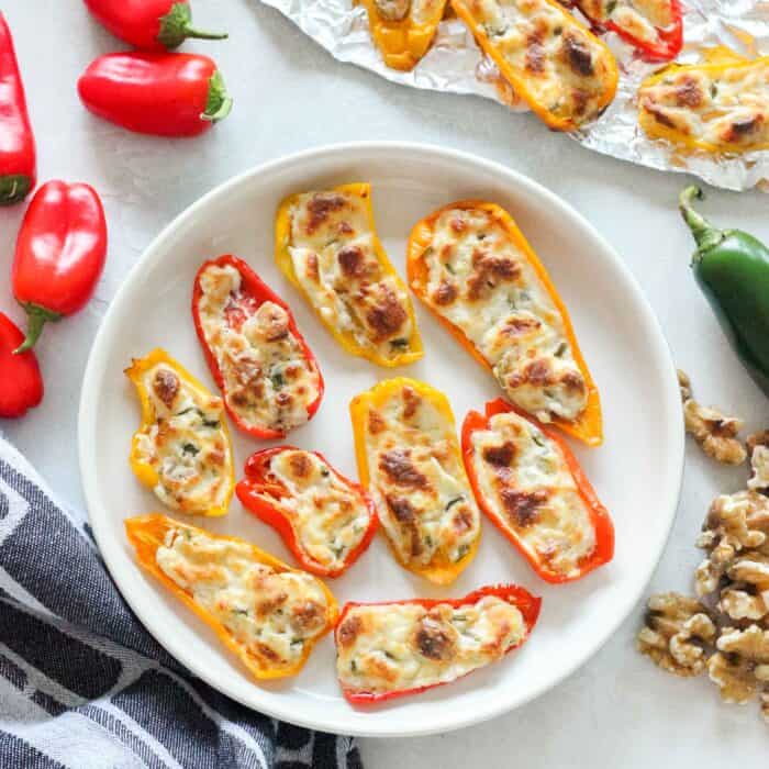 white plate with cream cheese stuffed peppers surrounded by baby bell peppers, walnuts, jalapeno, and a napkin