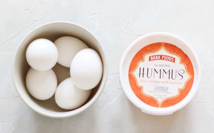 bowl of hard boiled eggs and a container of red pepper hummus
