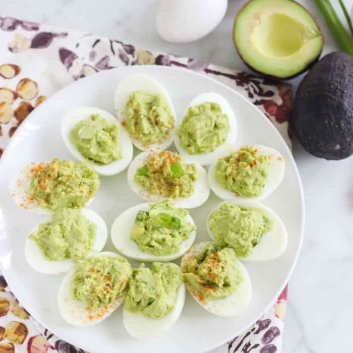 cut avocado, hard-boiled eggs, and a white plate on patterned napkin with avocado deviled eggs