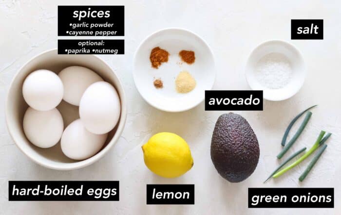 bowl of hard-boiled eggs, bowl of nutmeg, cayenne pepper, garlic powder, and paprika, lemon, avocado, green onion, and bowl of salt