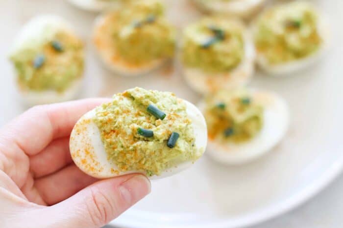 hand holding an avocado deviled egg over a plate of deviled eggs