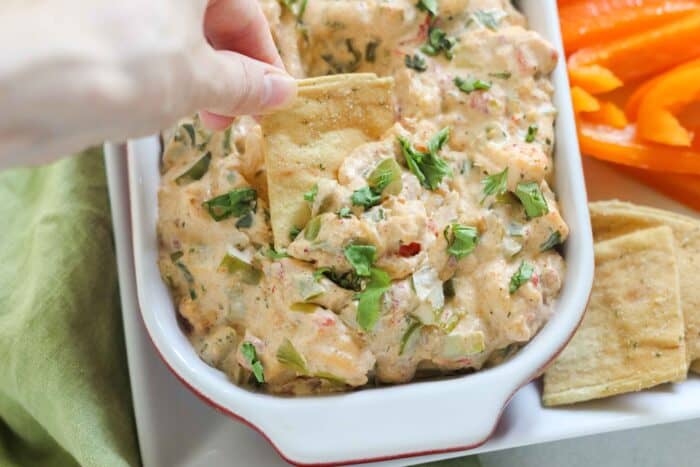 hand dipping a pita chip into a serving dish with crawfish dip