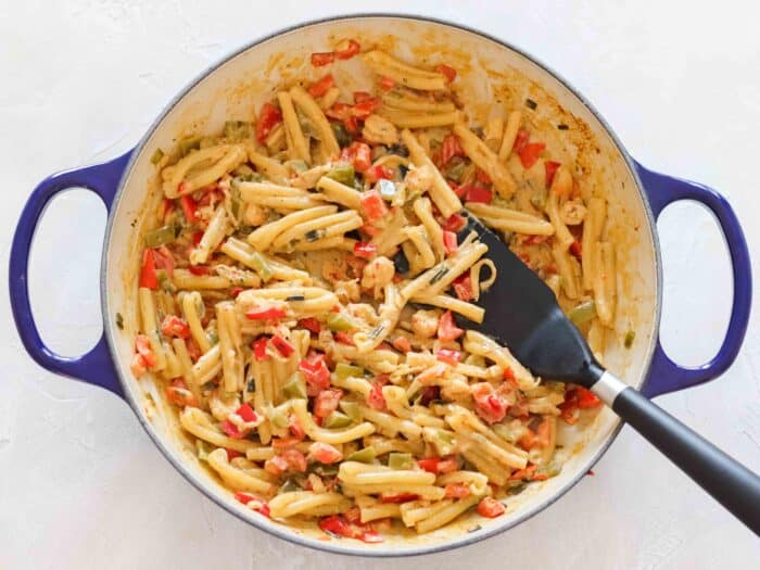 blue braiser with pasta and crawfish dip with a black spatula on a white counter