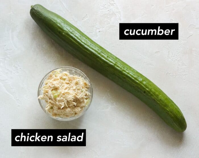 small bowl of chicken salad, large english cucumber on a white counter with text overlay describing ingredients