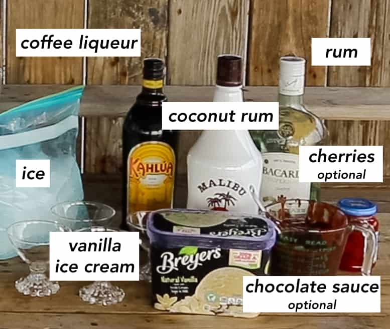 wooden table with a bag of ice, carton of vanilla ice cream, jar of cherries, jar of chocolate sauce, and bottles of kahlua, coconut rum, and silver rum