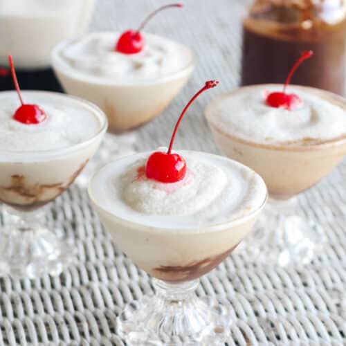 four glasses with frozen cocktail topped with cherries on a white wicker table