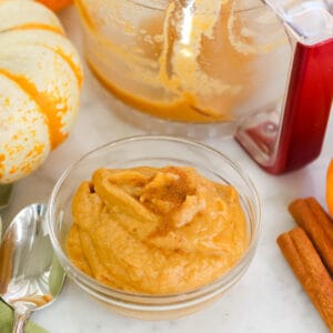 silver spoon, mini food processor bowl, small pumpkins, and a clear bowl with pumpkin banana ice cream sprinkled with cinnamon