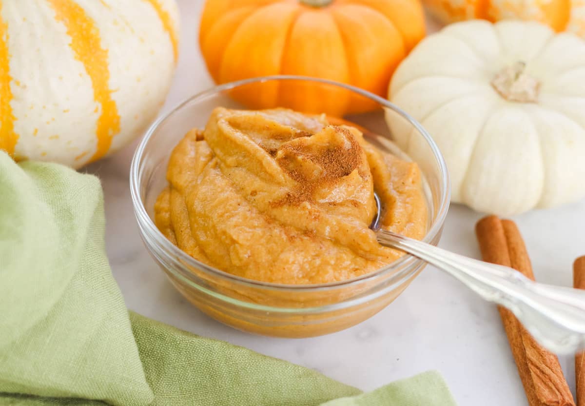 green napkin, small white and orange pumpkins, and a bowl of pumpkin ice cream sprinkled with cinnamon with a silver spoon