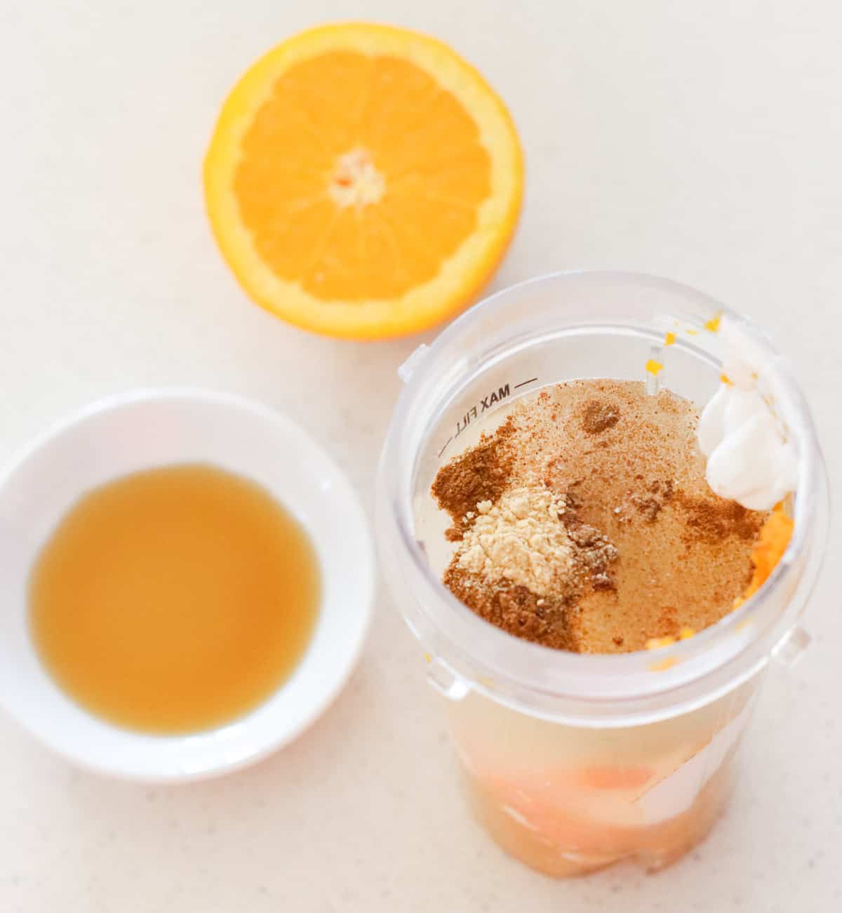 cut orange, bowl of maple syrup, smoothie cup with spices, water, yogurt, and pumpkin