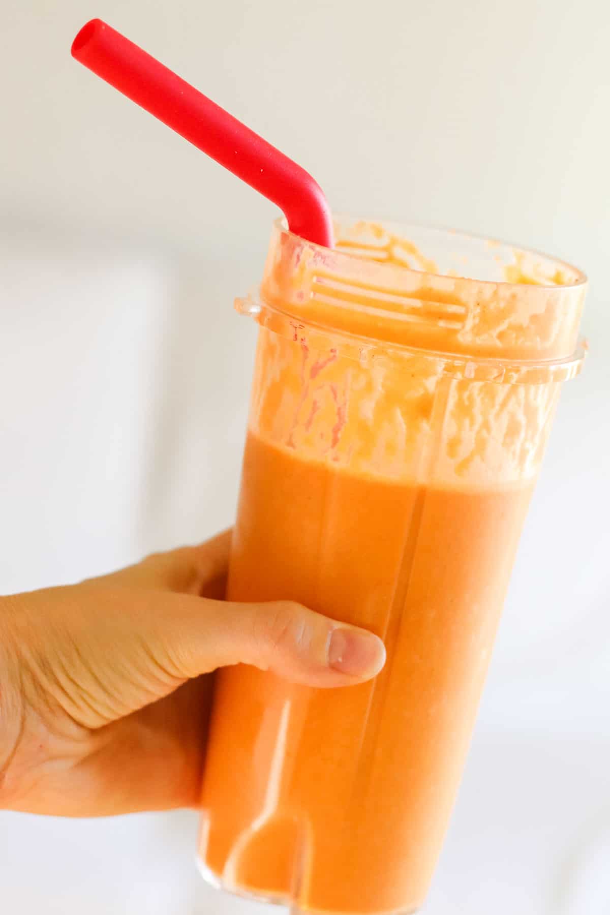 hand holding an orange smoothie with a red straw