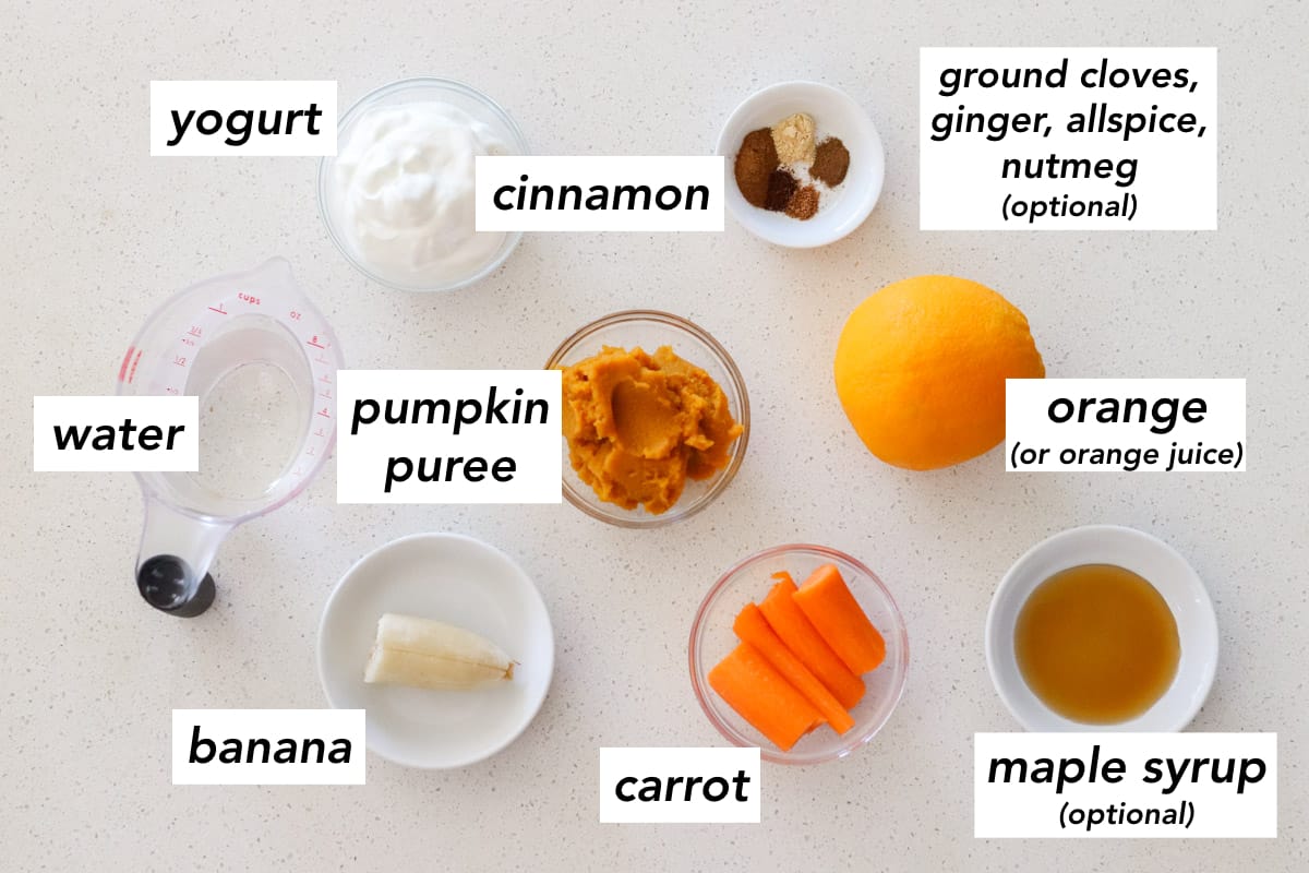 cup of water, bowl of yogurt, bowl with spices, bowl of pumpkin puree, half of a banana, bowl of chopped carrots, fresh orange, bowl with maple syrup