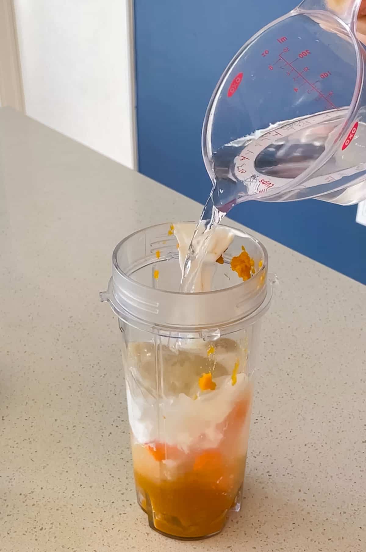 water pouring into a blender cup with pumpkin, yogurt, carrot, banana