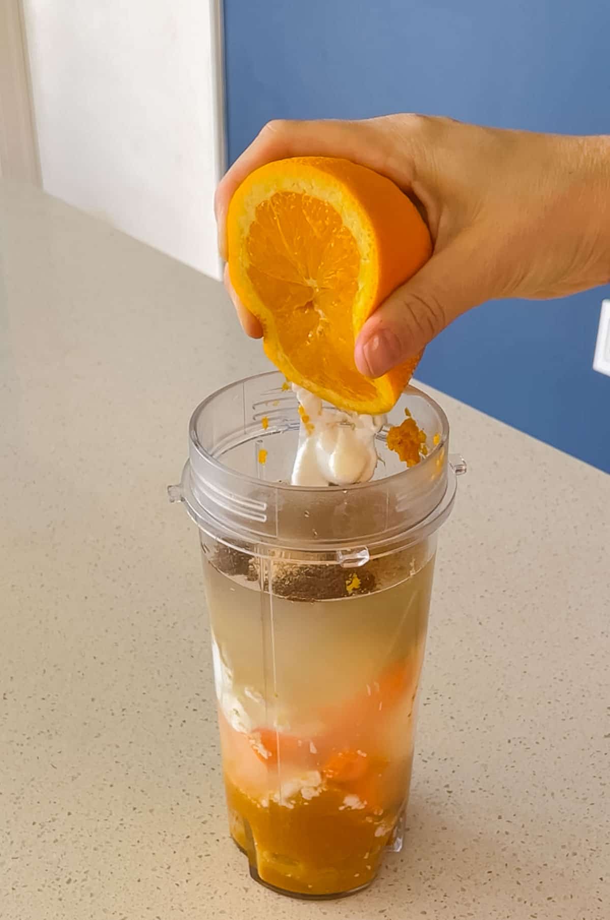 orange being squeezed into a blender cup full of yogurt, pumpkin, spices, water, carrot, banana