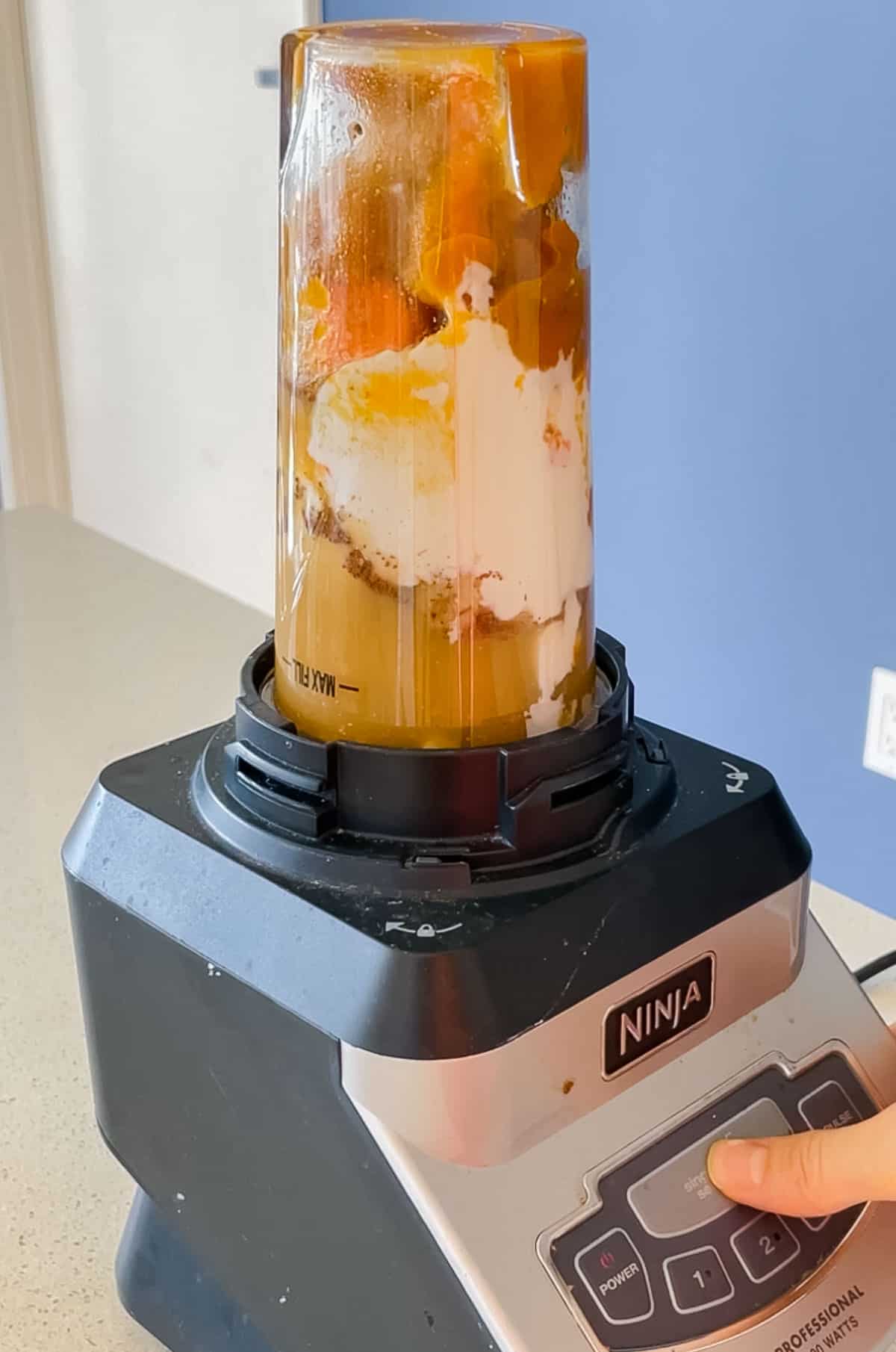 blender cup with carrot, pumpkin, spices, yogurt, and banana on a blender