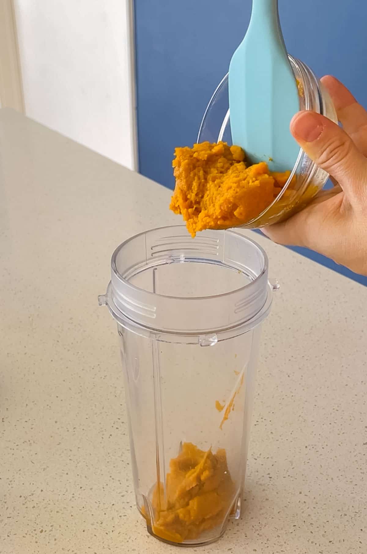 blue spatula pushes pumpkin puree out of a bowl into a blender cup