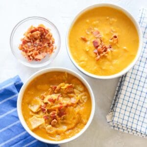 blue and white napkins under two bowls of pumpkin soup topped with bacon next to a small bowl of bacon