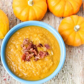 blue bowl of pumpkin soup topped with bacon next to small decorative pumpkins