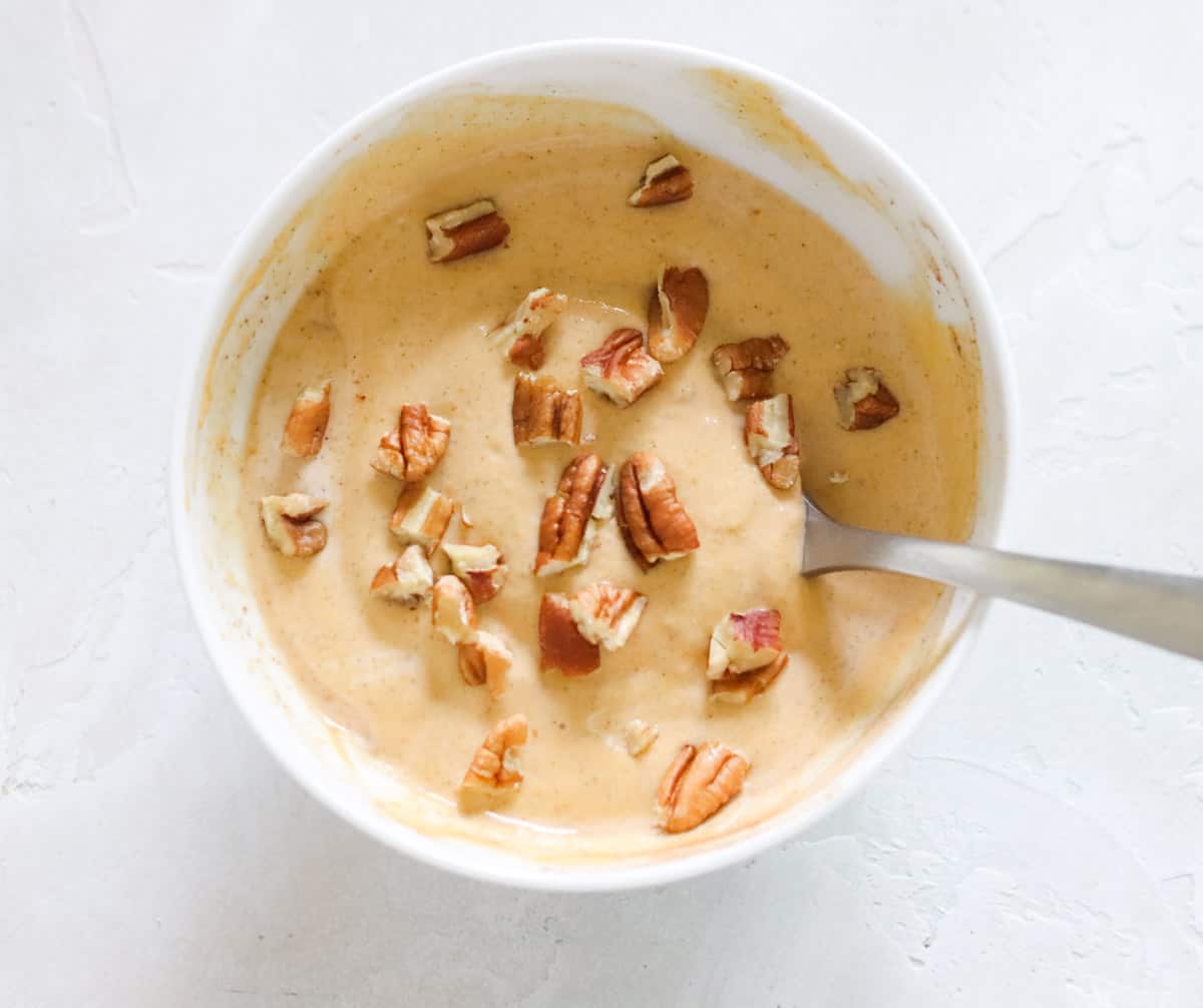 silver spoon in a white bowl of pumpkin yogurt topped with pecans